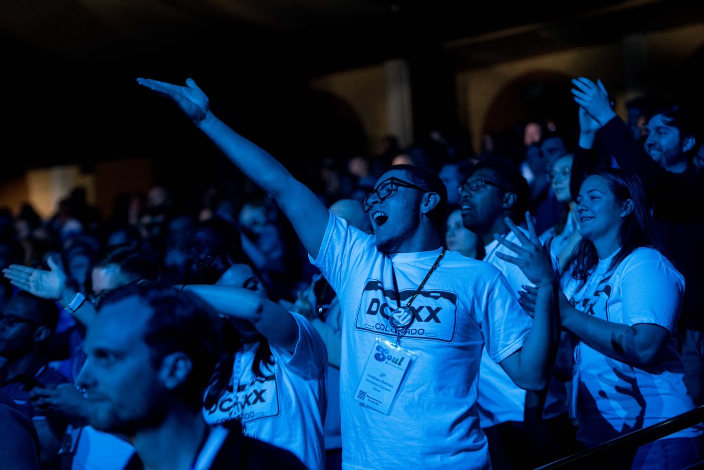 Employees cheering with arms raised in blue light during a general session