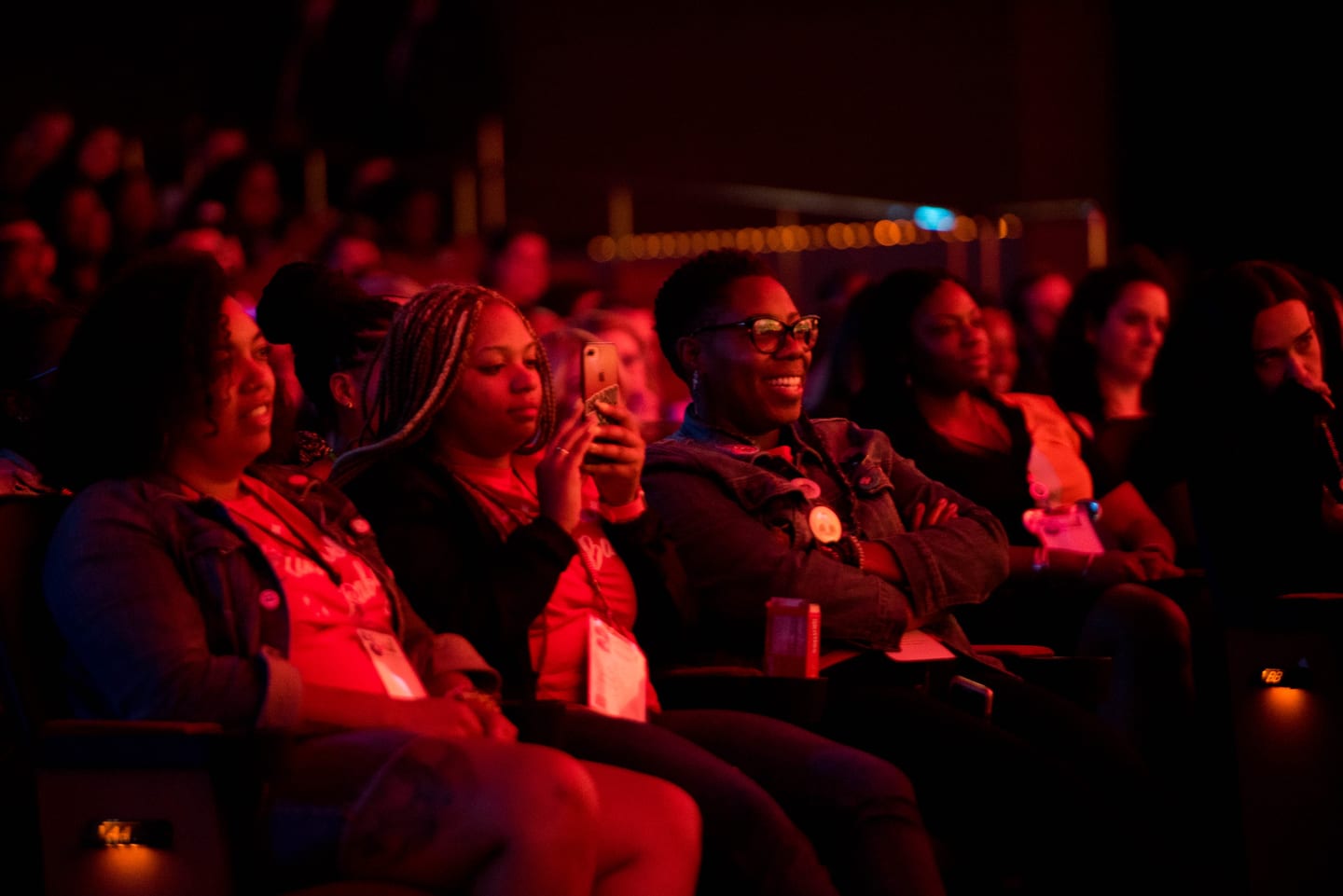 Rows of employees watching from the Colosseum seats under deep red stage light