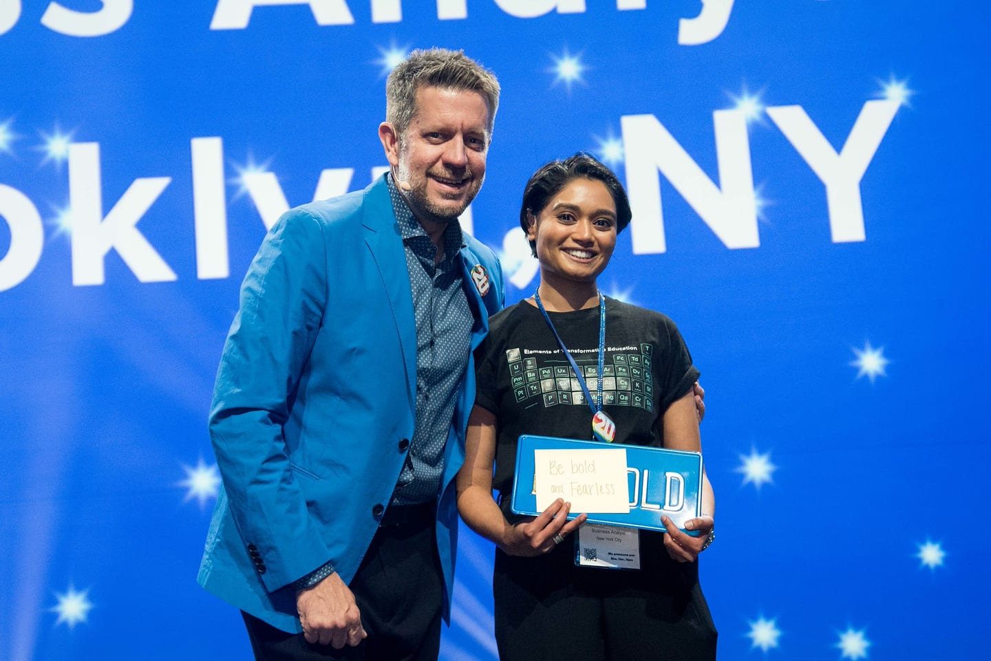 An executive presenting a certificate to an award recipient on the Colosseum stage against a blue screen