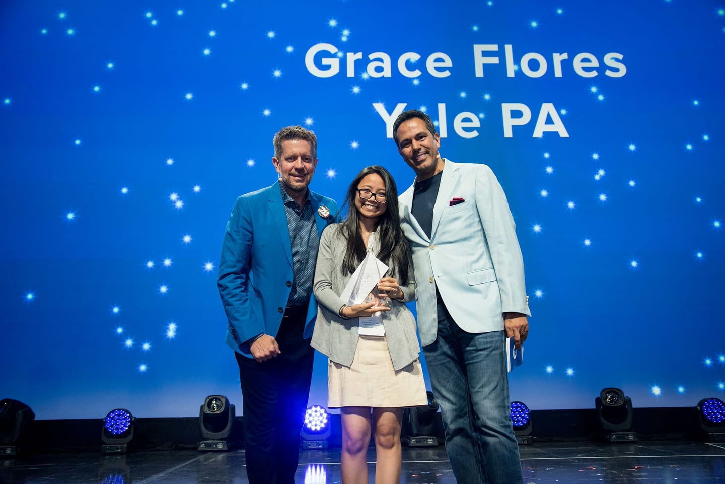 An award recipient photographed on stage between two executives beneath a starfield screen