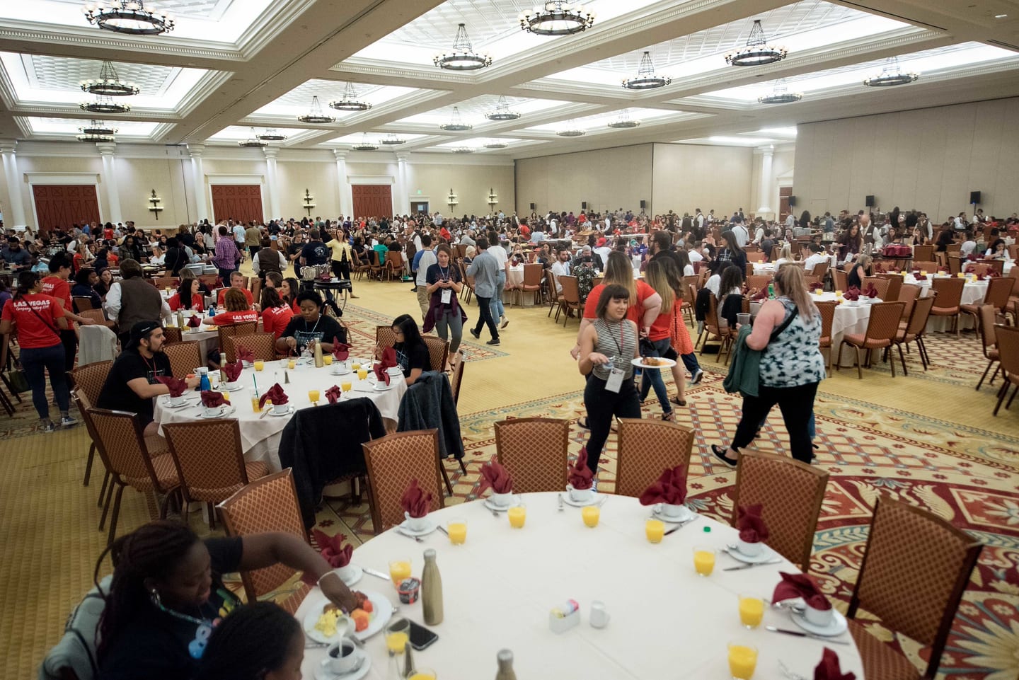 Employees finding seats at round tables in a ballroom before a session