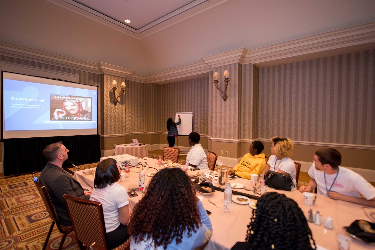 A breakout room at Caesars Palace with attendees seated at long tables facing a presenter and screen