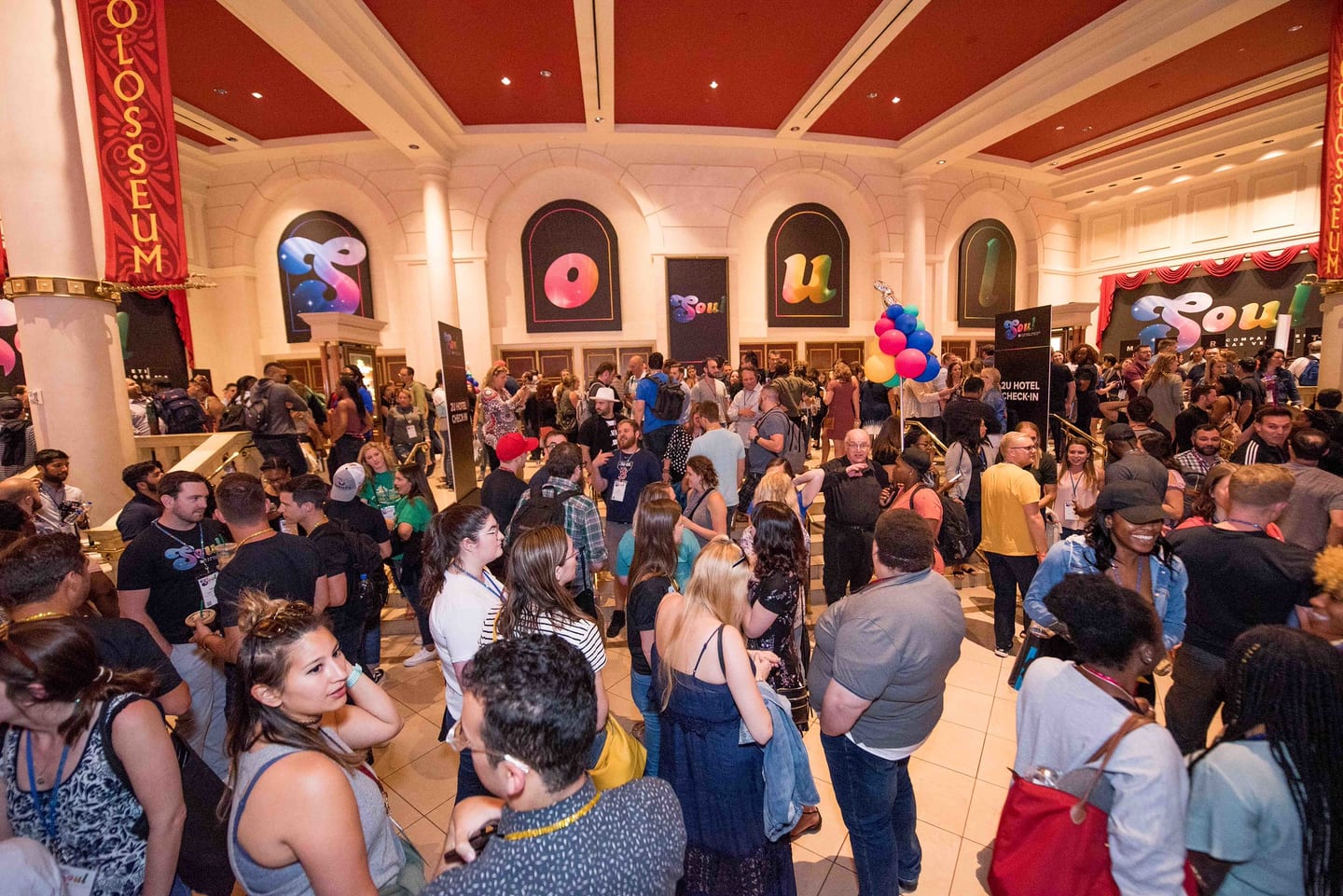 A crowd of employees filling the Colosseum lobby beneath its banners before a session