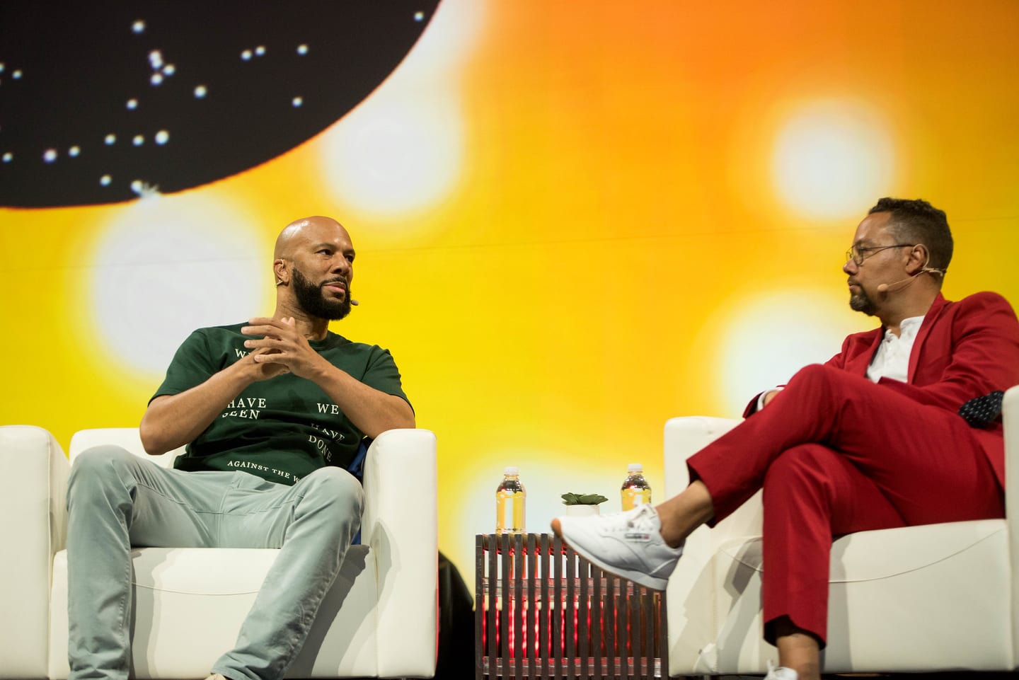 Common and his interviewer seated in white armchairs on stage under warm screen light