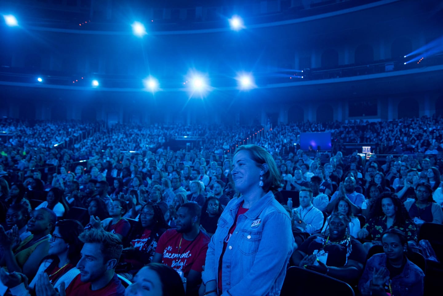 The audience seen from the stage, a sea of faces lit blue across the Colosseum