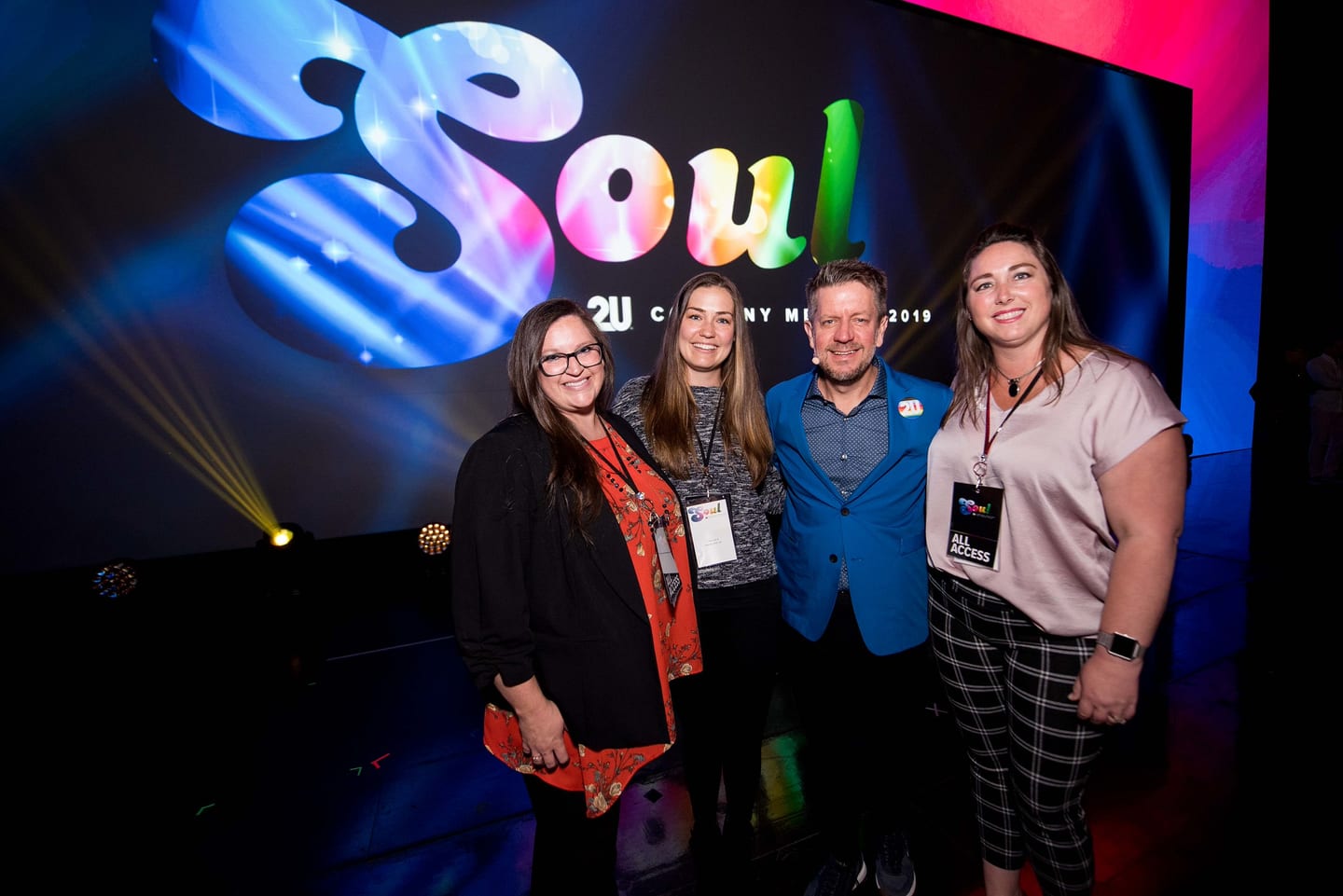 Four employees photographed together in front of the lit SOUL stage screen