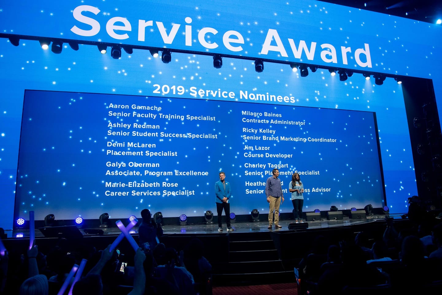 The Colosseum screen listing the 2019 Service Award nominees above a speaker on the darkened stage