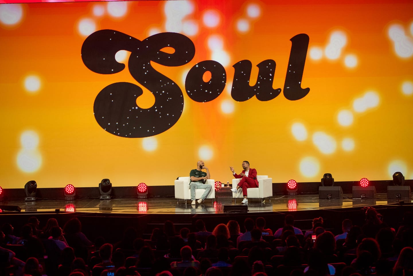 A wide view of the Colosseum stage showing a seated fireside conversation against a bright orange SOUL screen