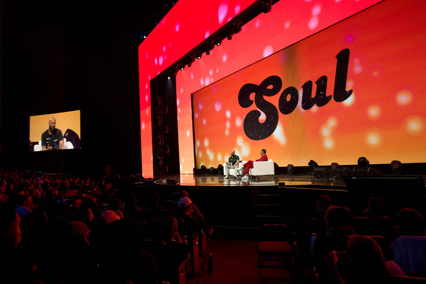 Two people seated on stage at the Colosseum in front of a deep red SOUL screen with the house in silhouette