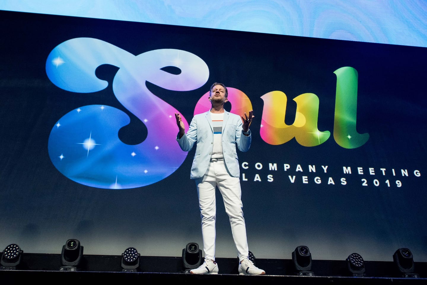 A speaker in a white suit alone on the Colosseum stage in front of the full-width SOUL 2U Company Meeting Las Vegas screen