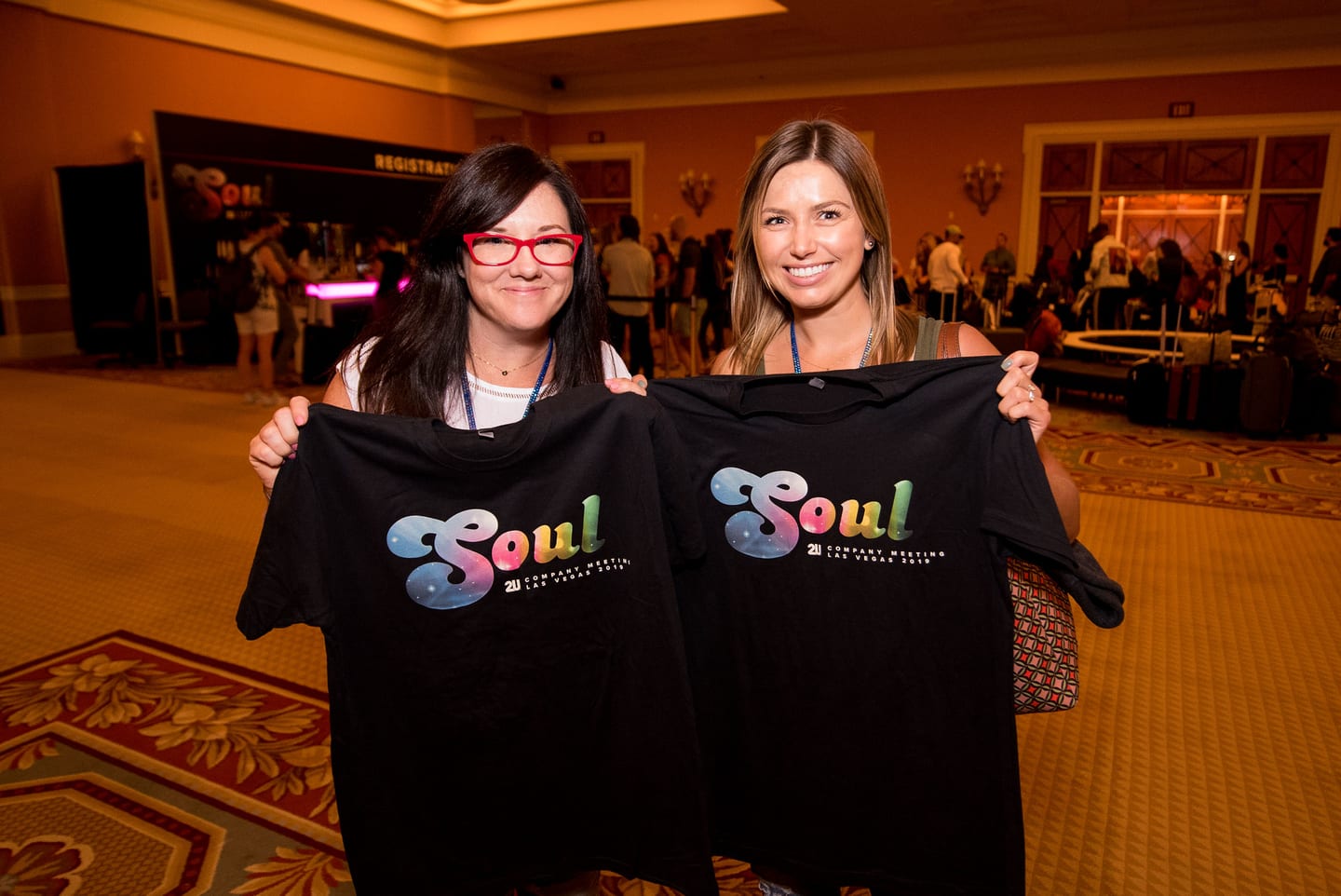Two employees holding up black SOUL company-meeting t-shirts