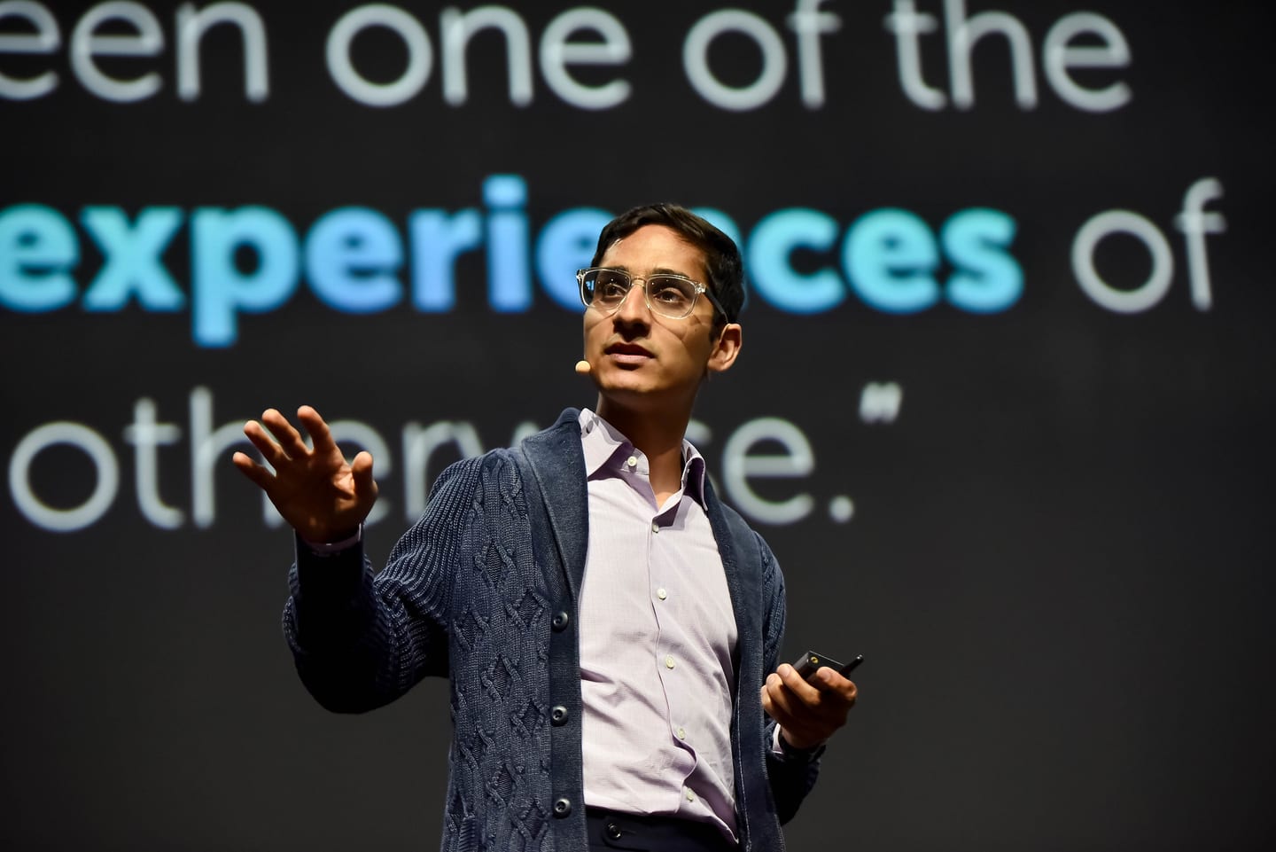 A speaker in a cardigan gesturing beneath a large pull-quote projected across the stage screen
