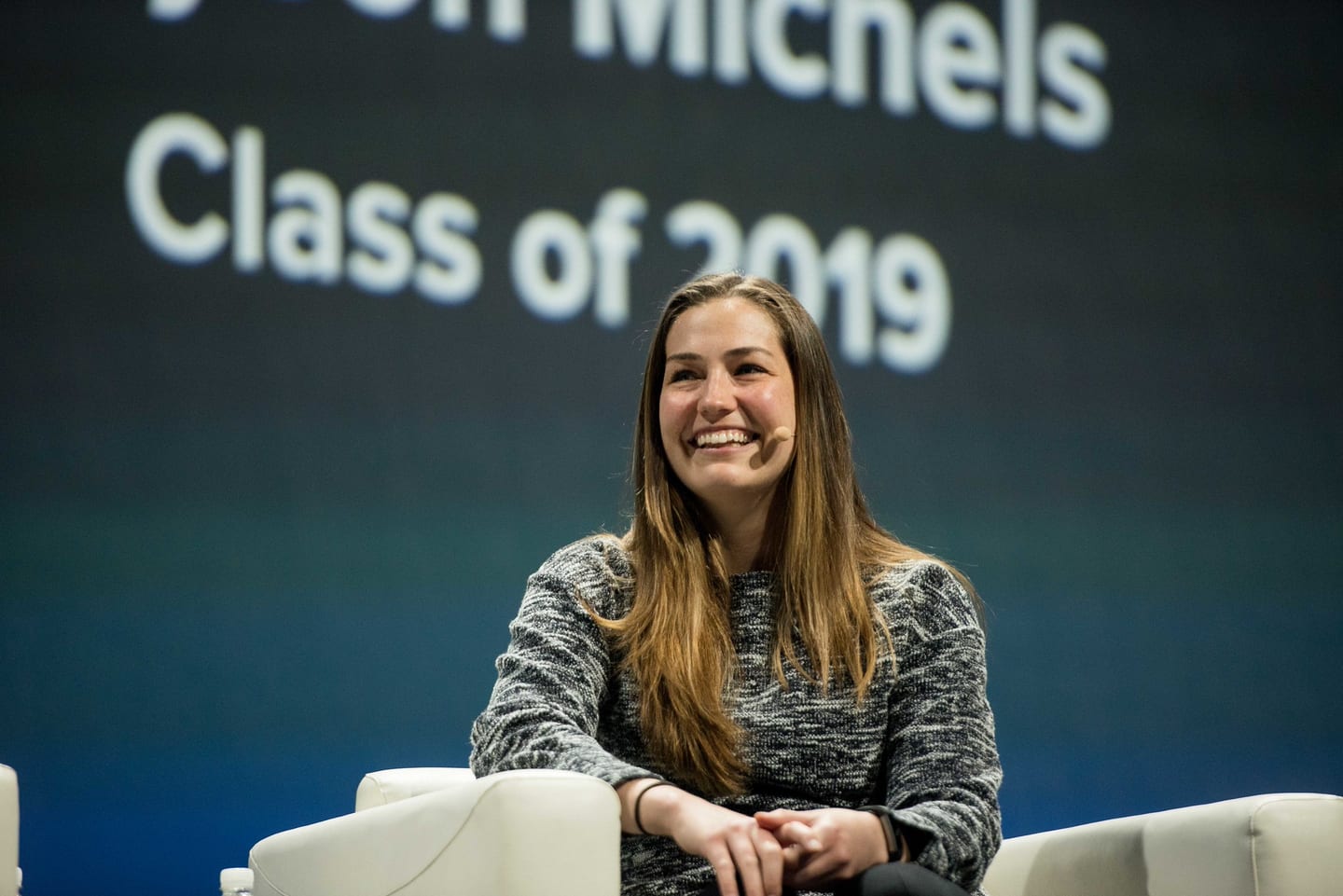 A seated speaker smiling in front of a screen reading Class of 2019