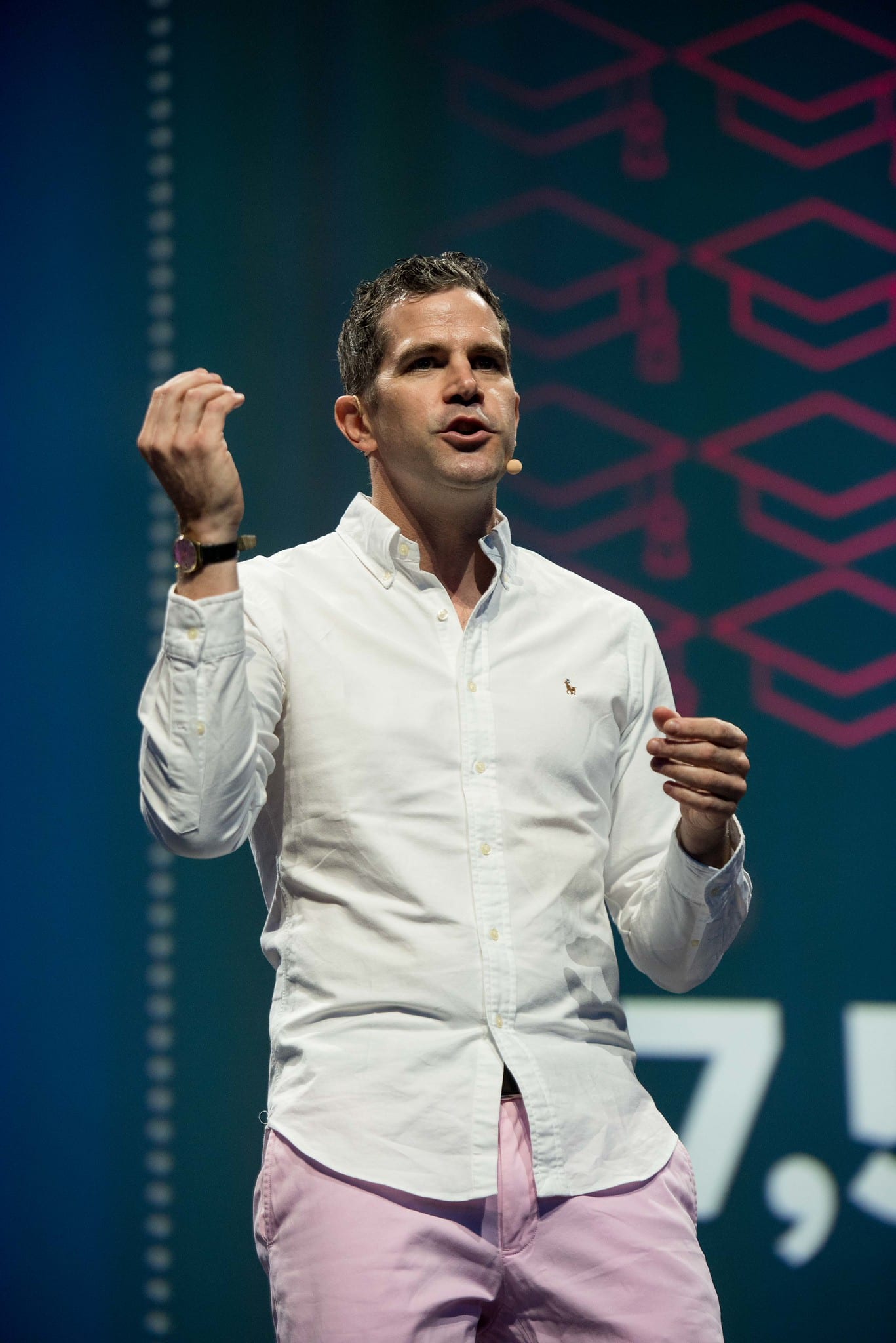 A speaker on stage with a fist raised in front of a magenta patterned screen