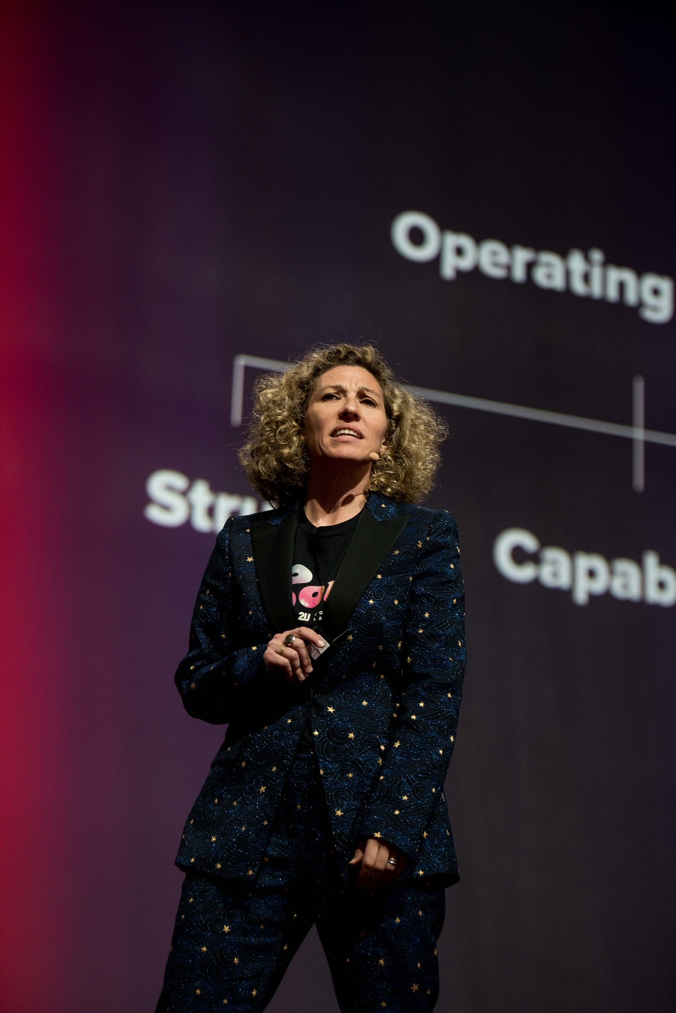 A speaker on stage beside a screen reading Operating Model, Structure and Capability