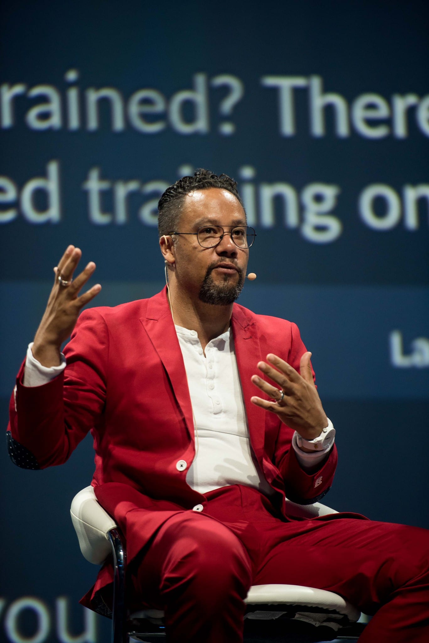 A host in a red suit seated on stage mid-sentence during a general session
