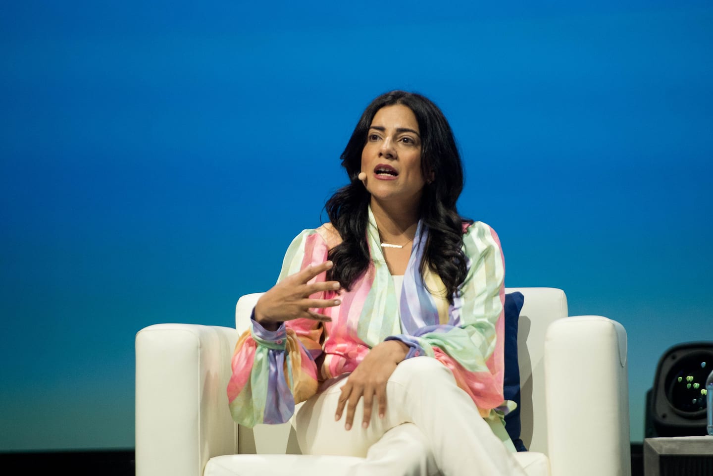 A speaker in a pastel jacket seated in a white armchair during an on-stage conversation