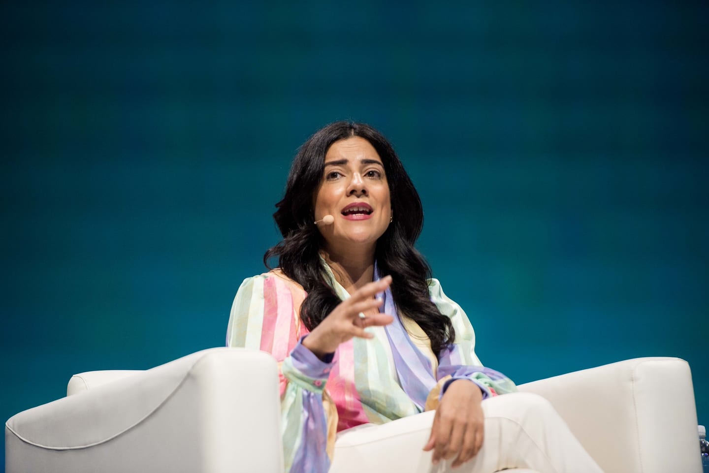 A speaker in a striped jacket seated in a white armchair during an on-stage interview
