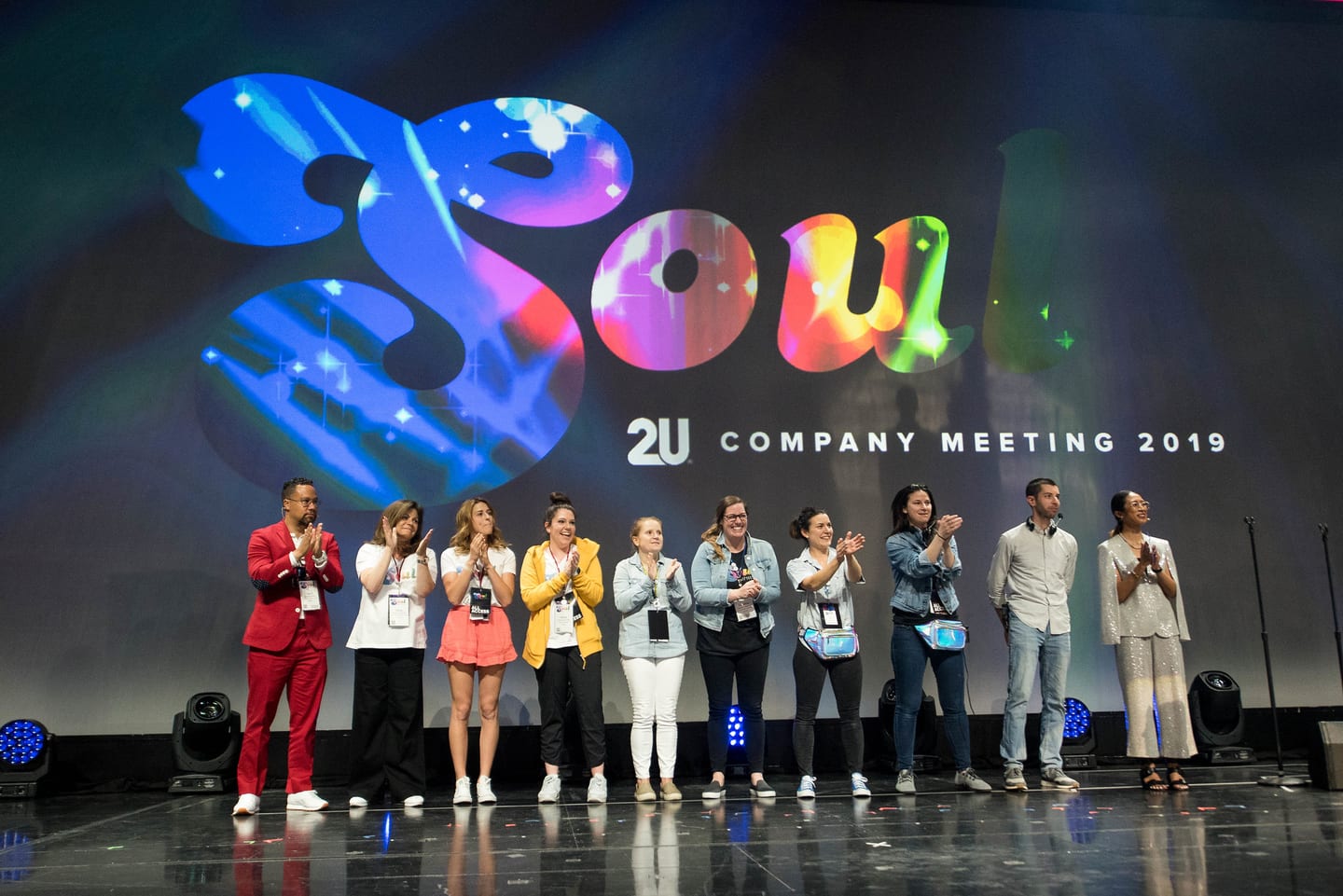 A group of employees applauding on stage in front of the SOUL 2U Company Meeting 2019 screen