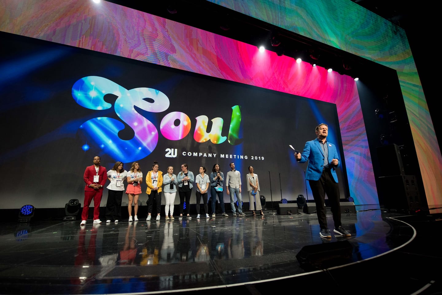 A line of employees standing across the Colosseum stage beside a host under the SOUL screen