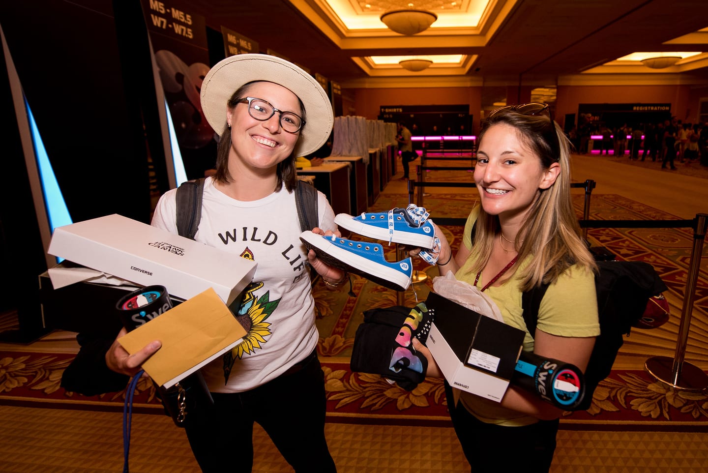 Two employees holding up boxed sneakers and branded items in a hotel corridor