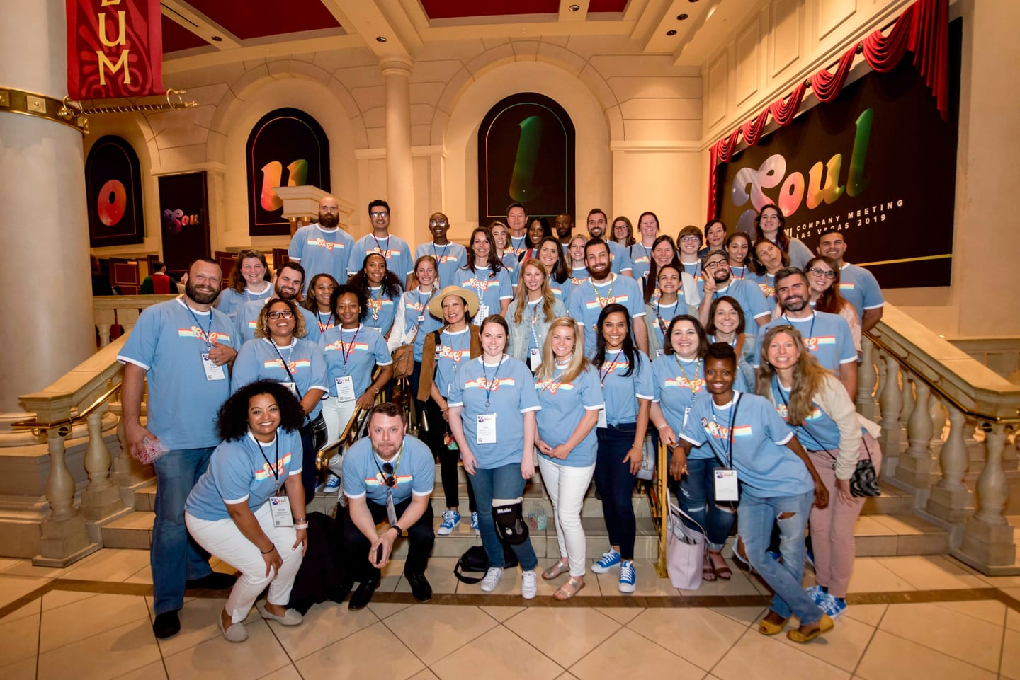 A large group of employees in blue 2U shirts posed on the marble staircase at Caesars Palace