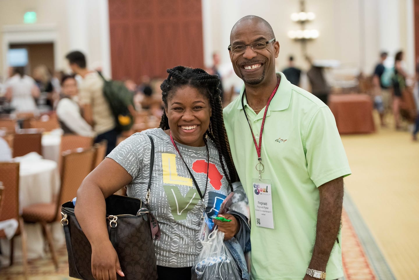 Two employees smiling together in a hotel corridor between sessions