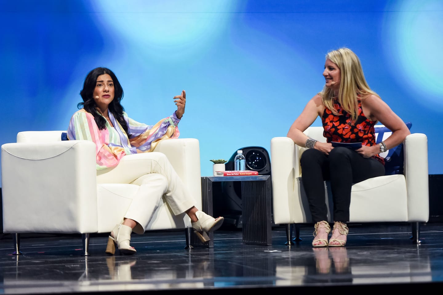Two speakers seated in white armchairs facing each other during an on-stage conversation