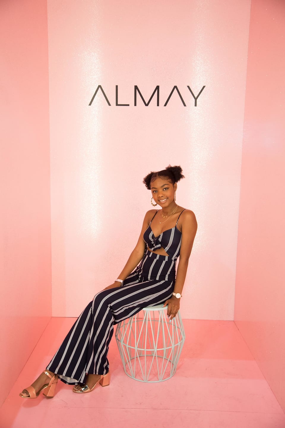 An influencer posing at an Almay beauty activation against a pink set with the Almay logo