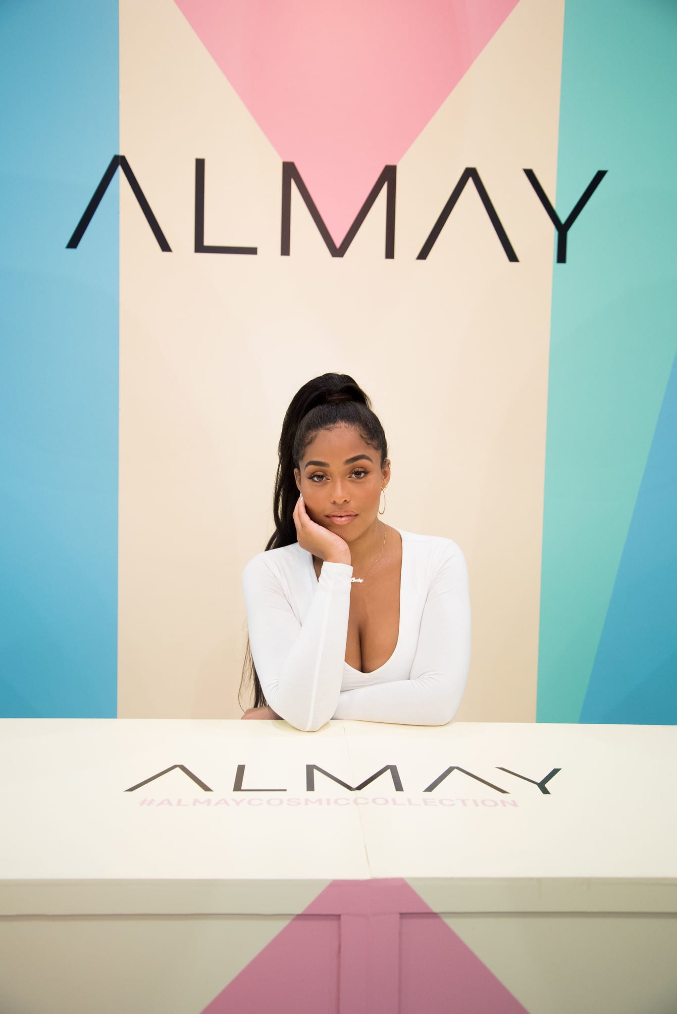 A guest posing at the counter in front of the geometric Almay Cosmic Collection backdrop at a beauty brand activation in Los Angeles