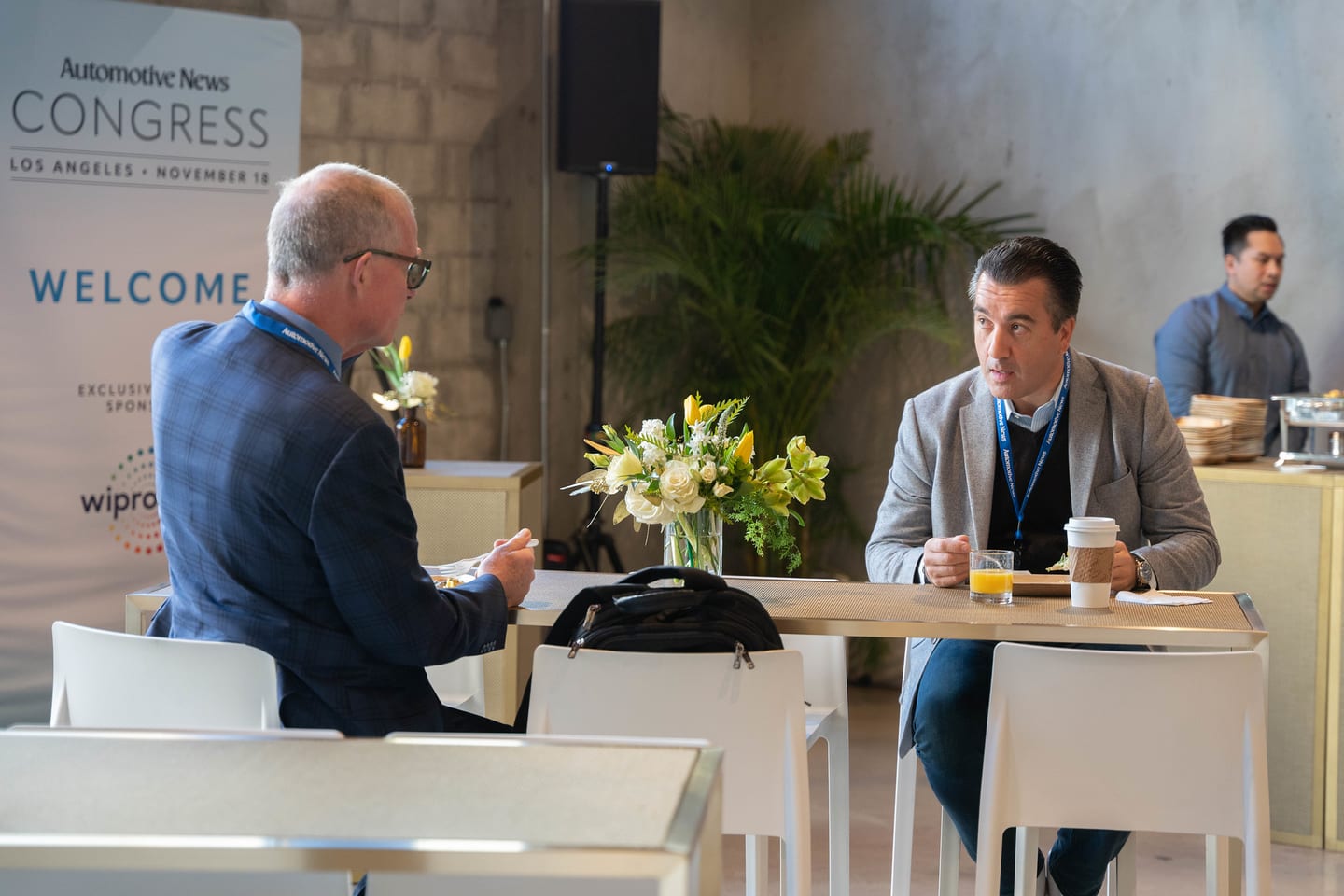 Two attendees at a breakfast table in front of the Welcome wall at the Automotive News Congress: Los Angeles, City Market Social House