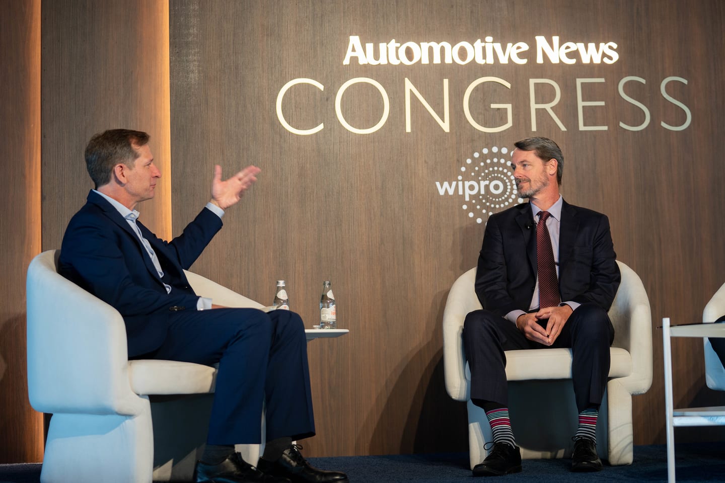 Two speakers in a fireside conversation beneath the illuminated Automotive News Congress wall at the Automotive News Congress: Los Angeles, City Market Social House