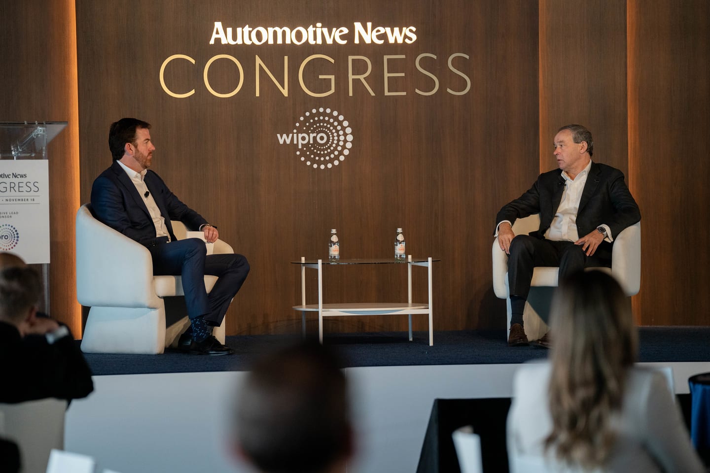 Two speakers in a fireside conversation beneath the Automotive News Congress and Wipro branding at the Automotive News Congress: Los Angeles, City Market Social House