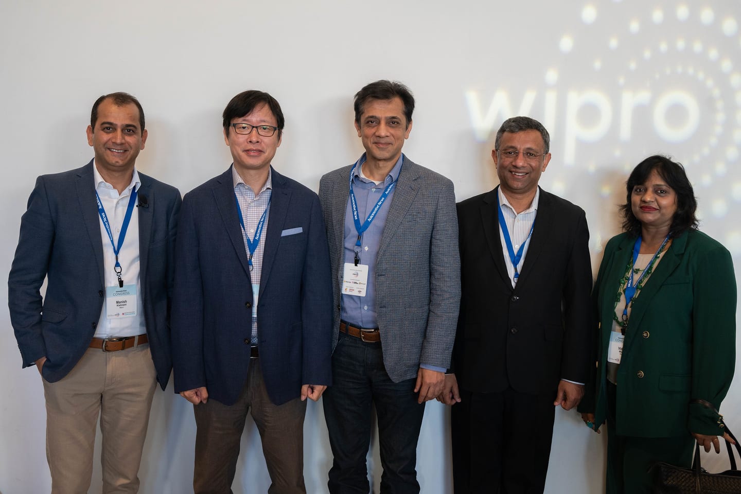 Five attendees posing together in front of the projected Wipro sponsor logo at the Automotive News Congress: Los Angeles, City Market Social House