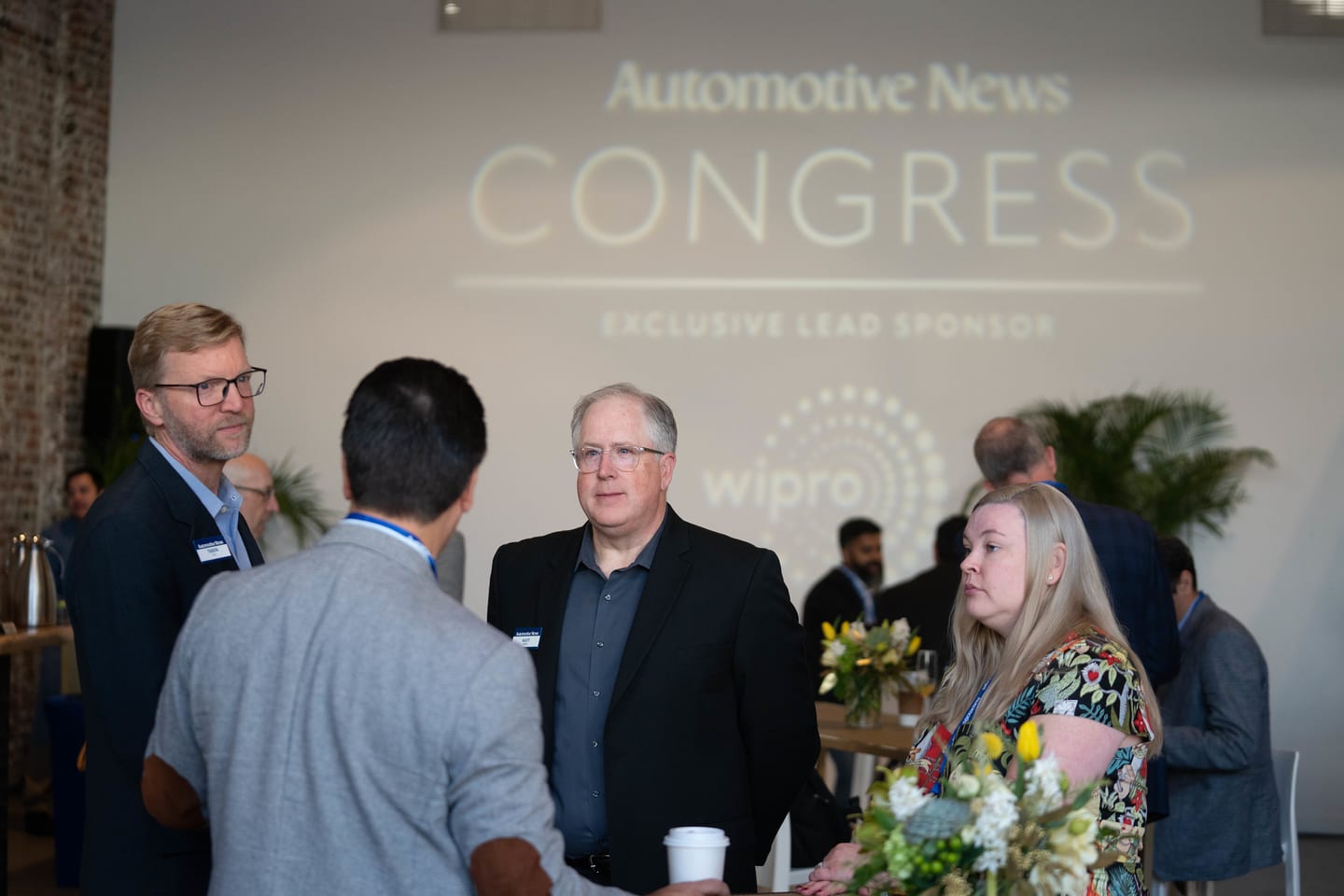 A group of attendees in conversation in front of the projected sponsor wall at the Automotive News Congress: Los Angeles, City Market Social House