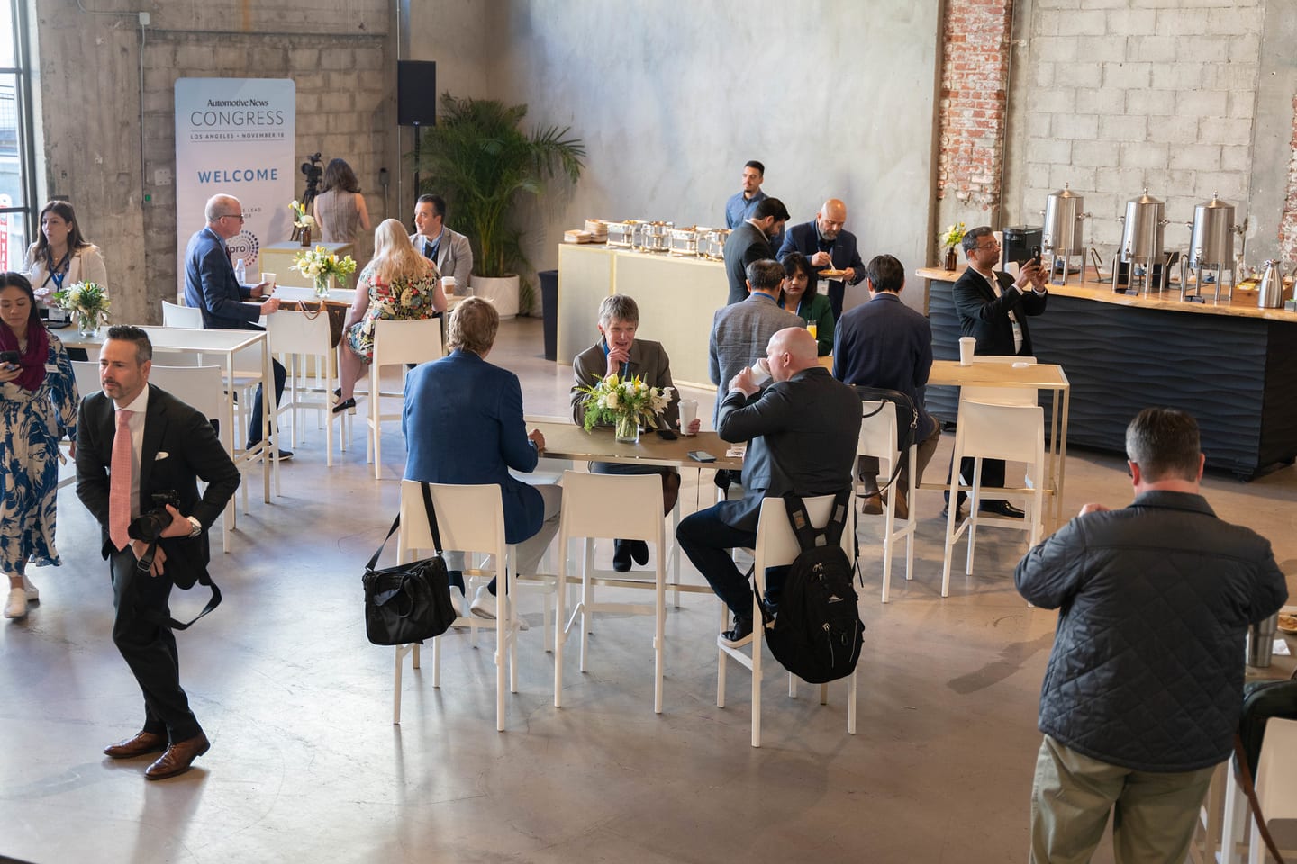 A wide view of the networking area with attendees at high tables in front of the Welcome wall at the Automotive News Congress: Los Angeles, City Market Social House