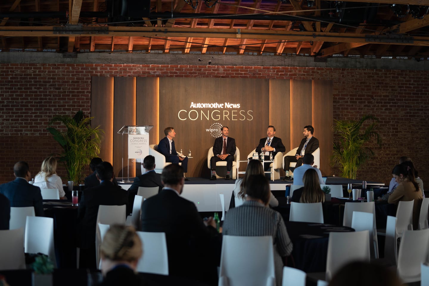 A panel on stage seen past the heads of the seated audience at the Automotive News Congress: Los Angeles, City Market Social House