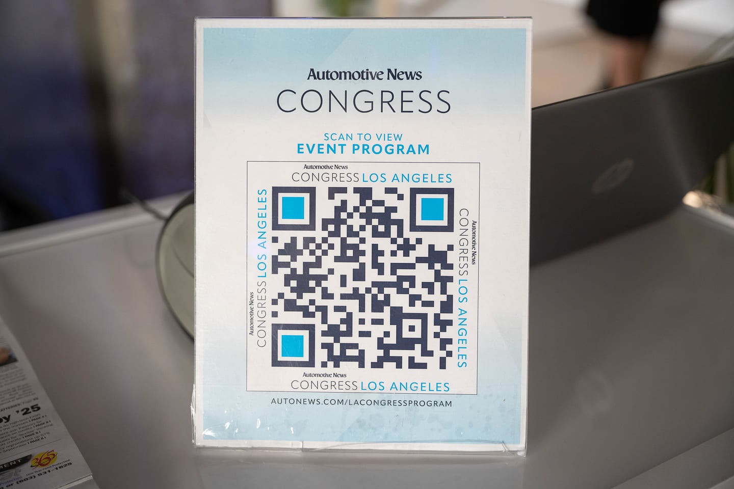 A printed Automotive News Congress event-program card with a QR code standing on a table beside a laptop at the Automotive News Congress: Los Angeles, City Market Social House