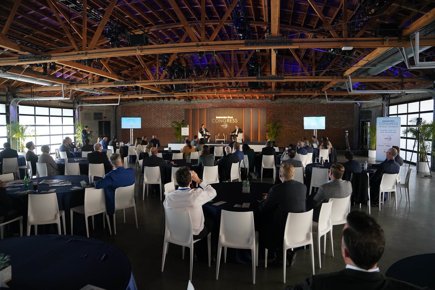 A wide view of the room and its exposed timber roof trusses, set with round tables at the Automotive News Congress: Los Angeles, City Market Social House