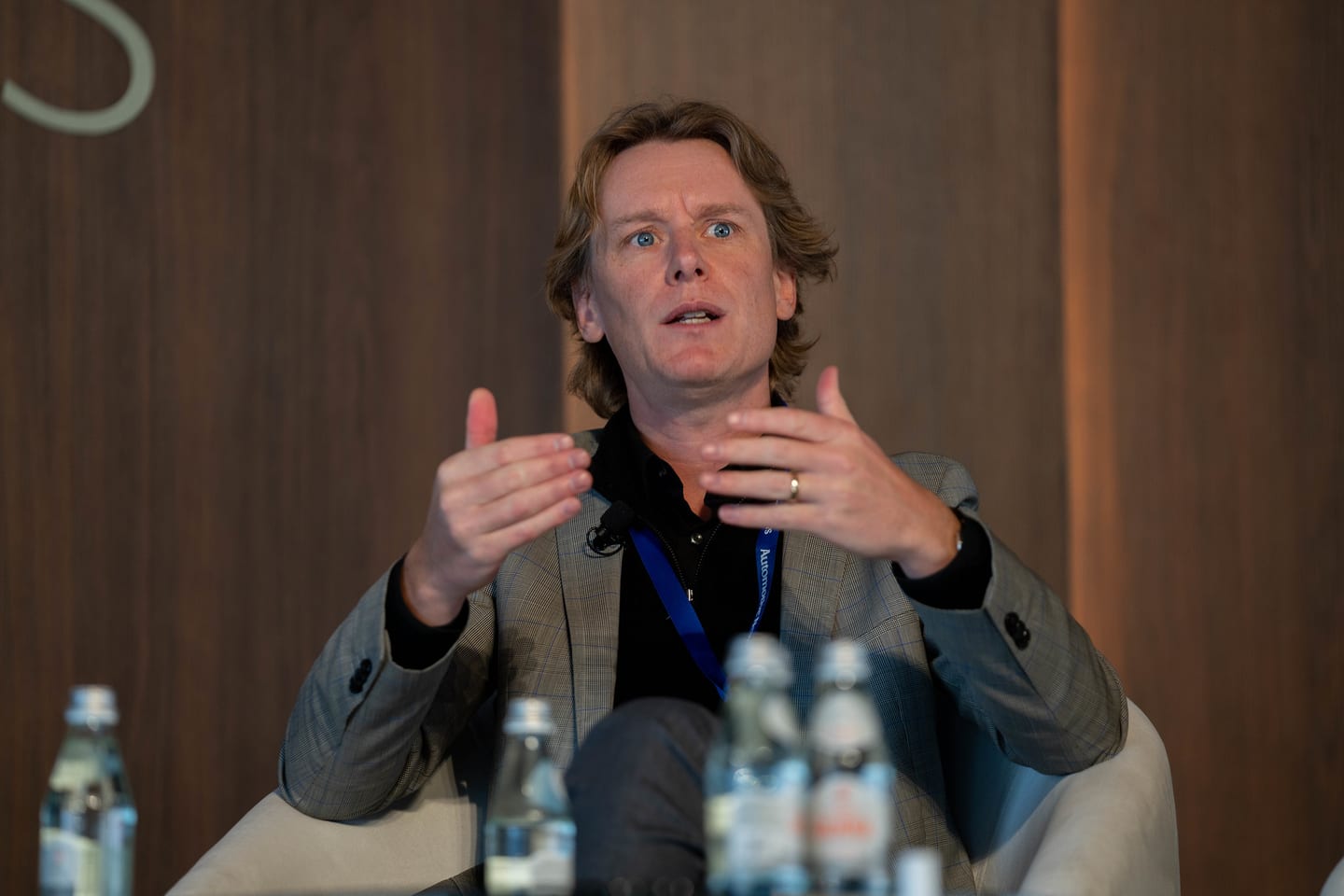 A speaker gesturing with both hands mid-answer during a stage session at the Automotive News Congress: Los Angeles, City Market Social House