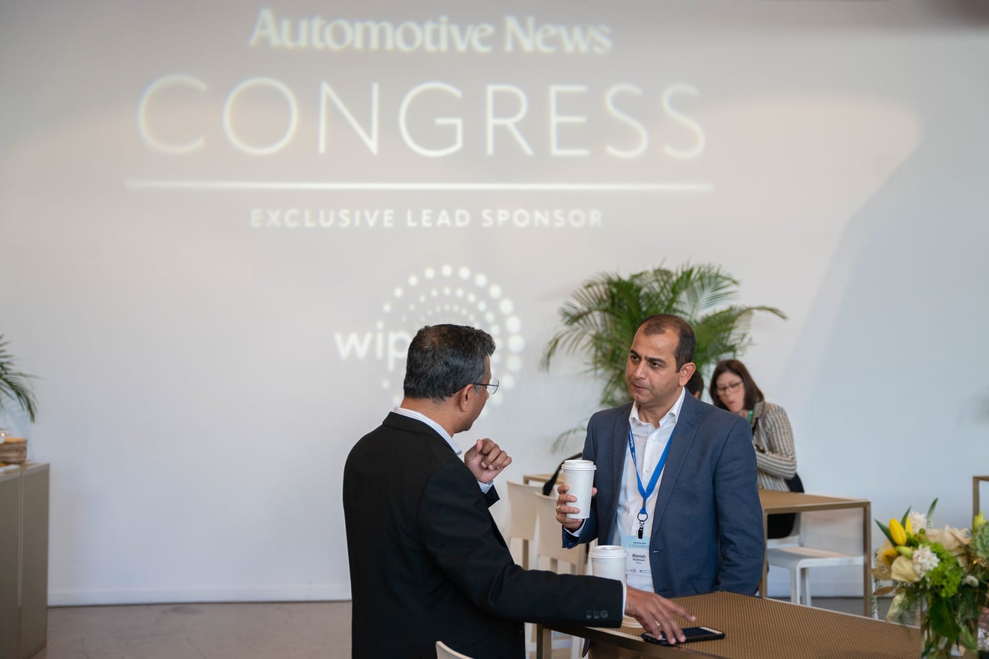 Two attendees talking in front of the projected exclusive-lead-sponsor wall at the Automotive News Congress: Los Angeles, City Market Social House