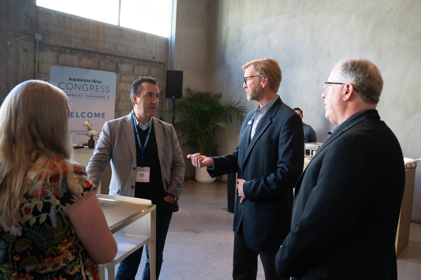 Three attendees in conversation in front of the Welcome wall at the Automotive News Congress: Los Angeles, City Market Social House