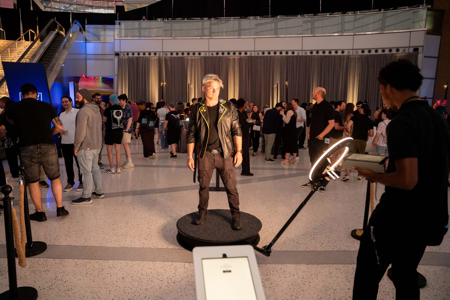 A guest in a leather jacket standing on a 360 video booth platform beside a ring light, with the crowd behind him