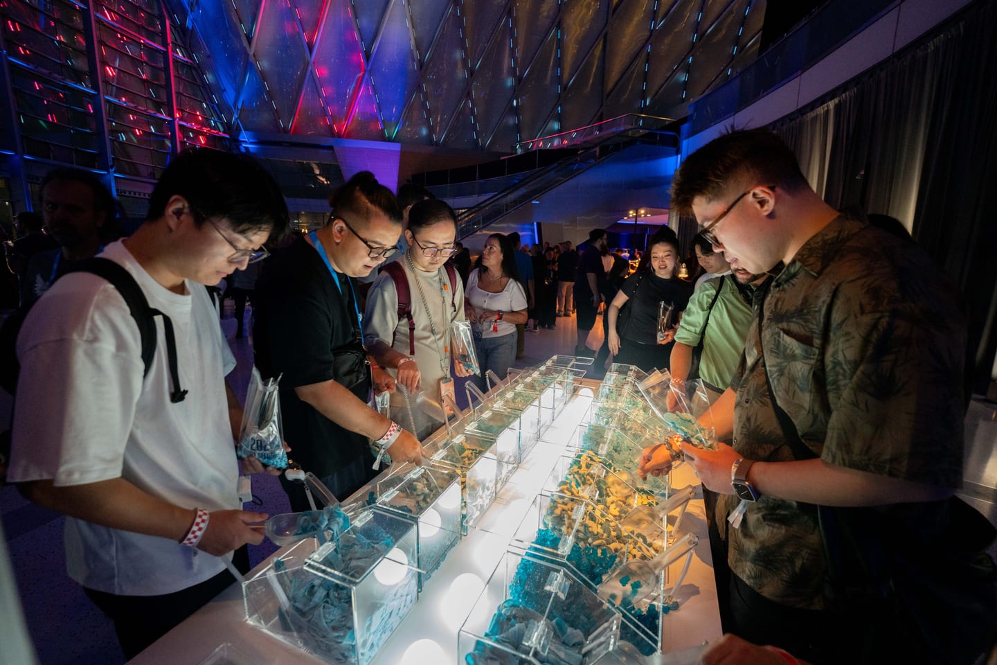 Guests scooping blue and yellow candy from a lit acrylic candy bar under the ARTIC roof