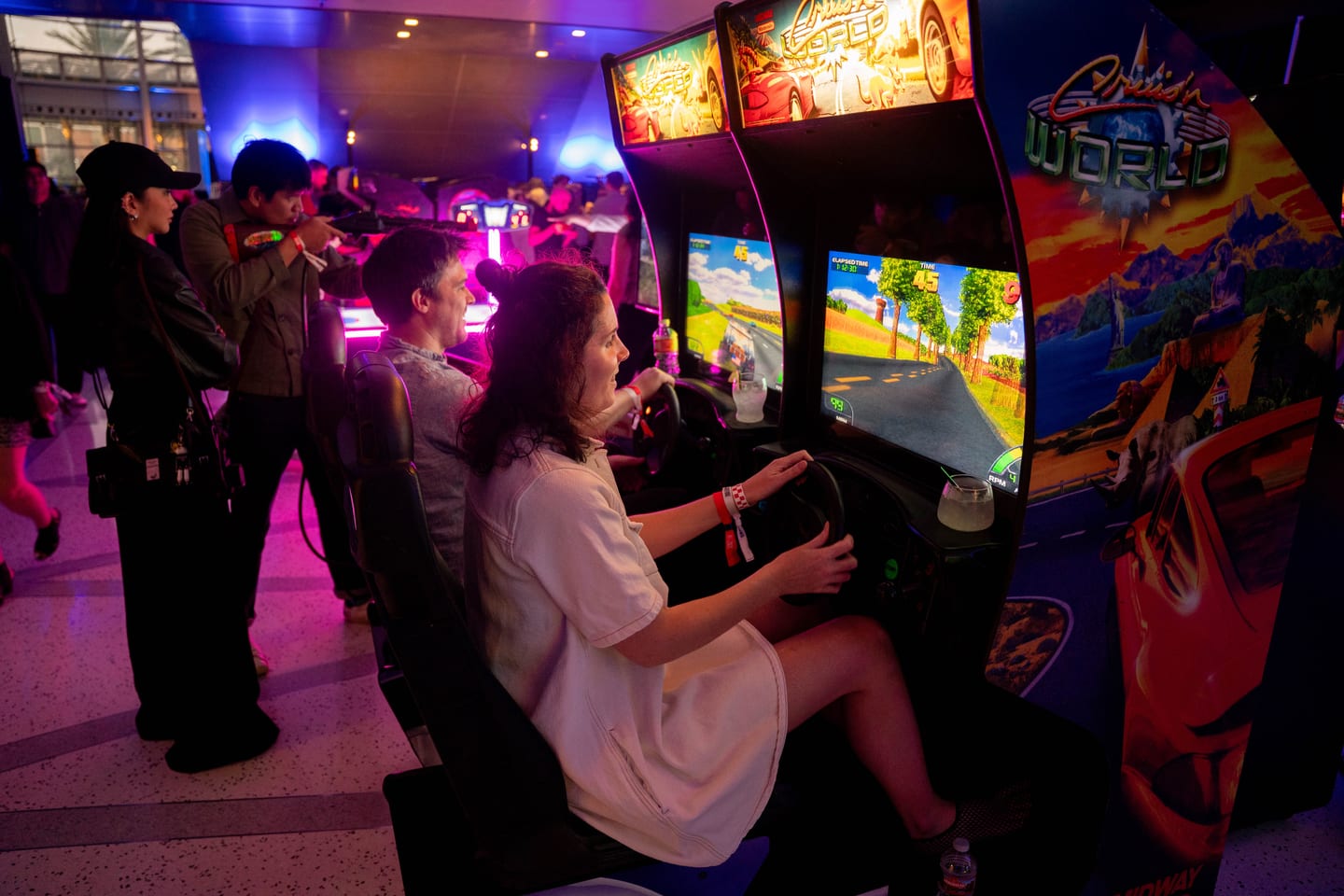 A guest gripping the wheel of a driving arcade cabinet while others watch