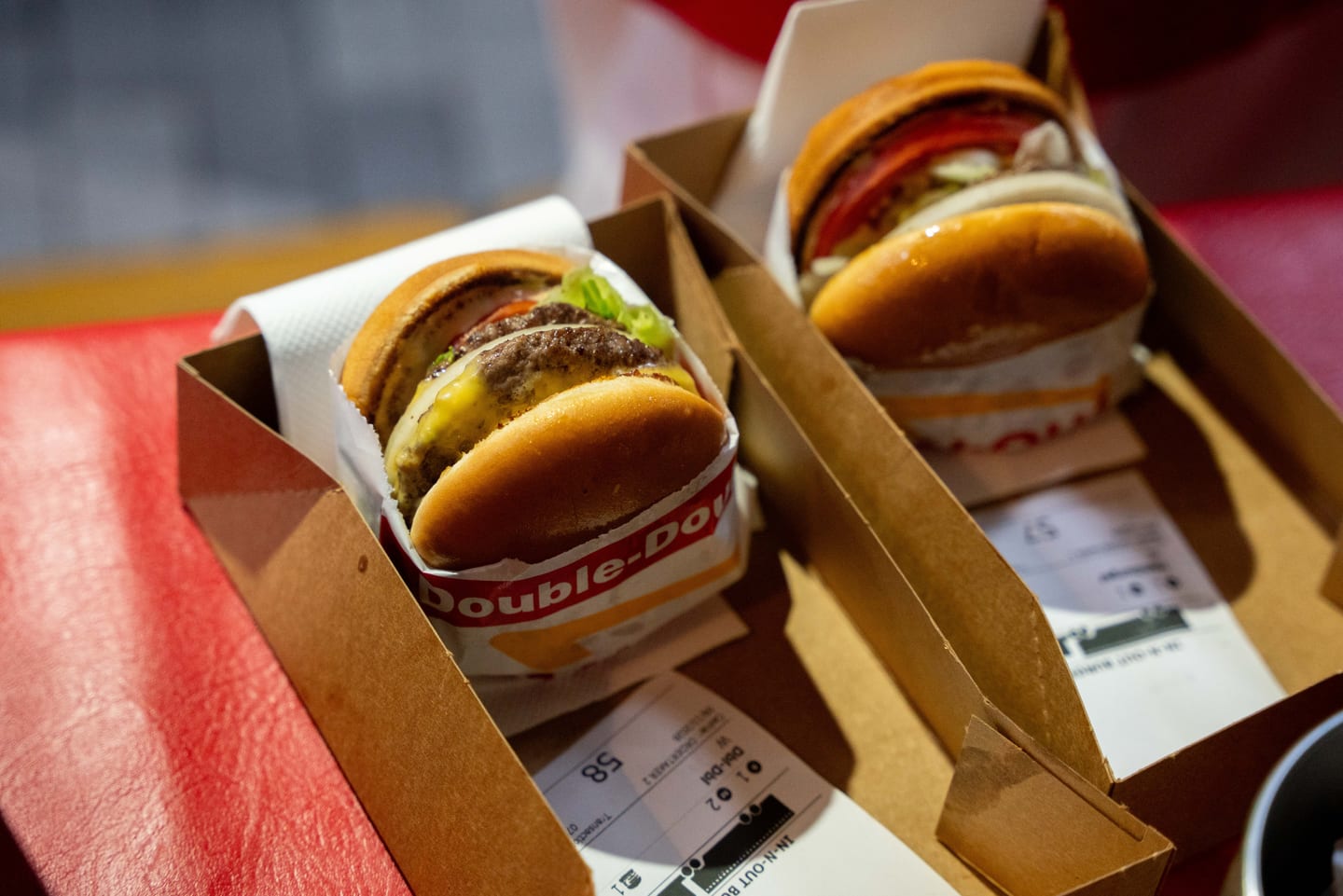 Two In-N-Out Double-Double burgers in paper boats on a red counter