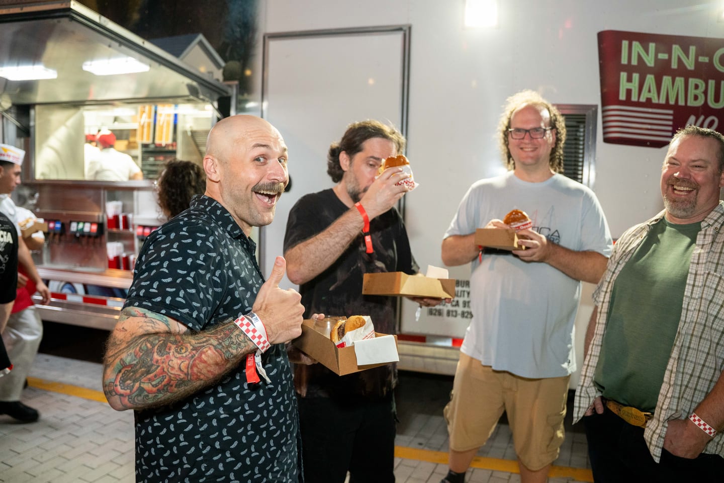 Guests holding In-N-Out burgers in front of the In-N-Out truck, one giving a thumbs up