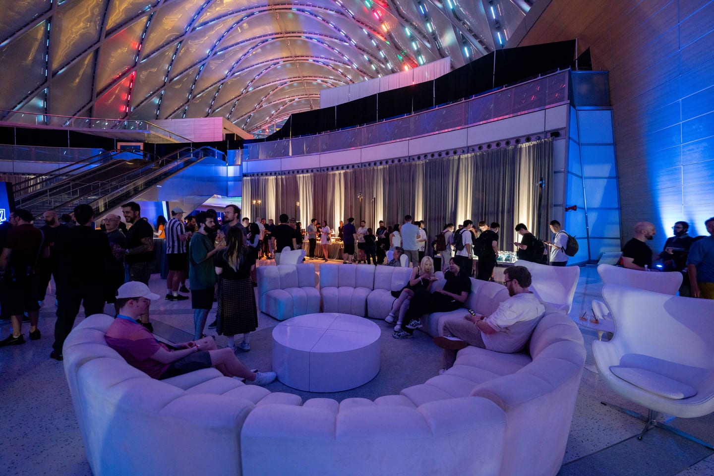 Guests on curved white sofas in a lounge area beneath the lit arched roof of ARTIC