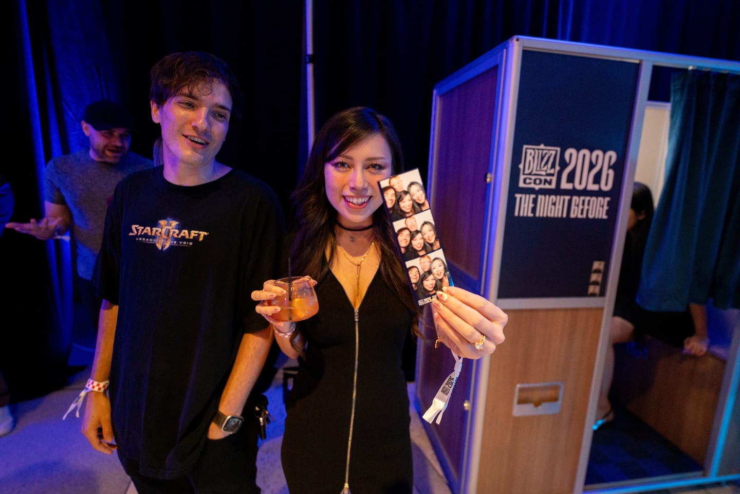 A guest holding up a photo strip next to a booth branded BlizzCon 2026 The Night Before