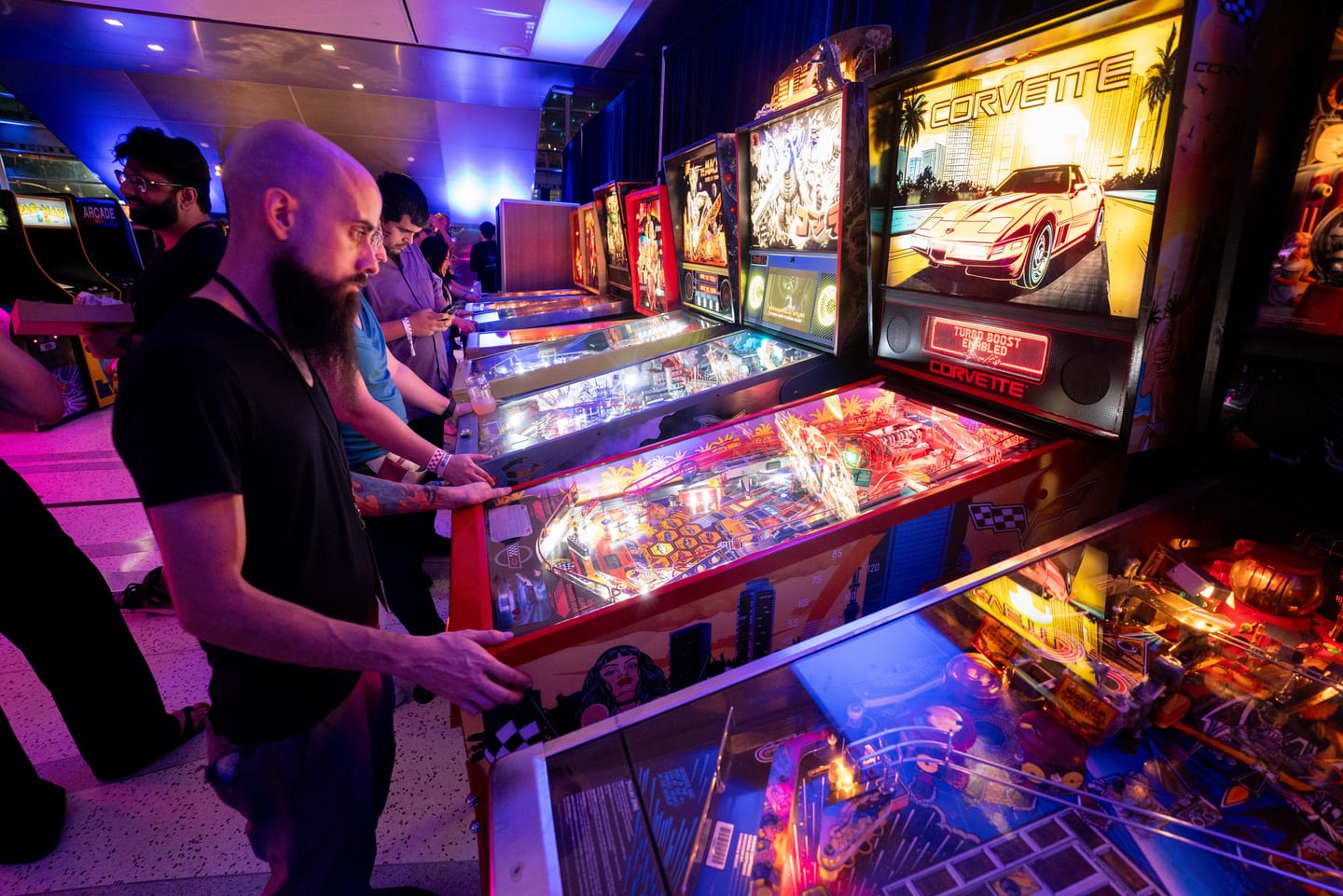 Guests playing a row of lit pinball machines in the arcade